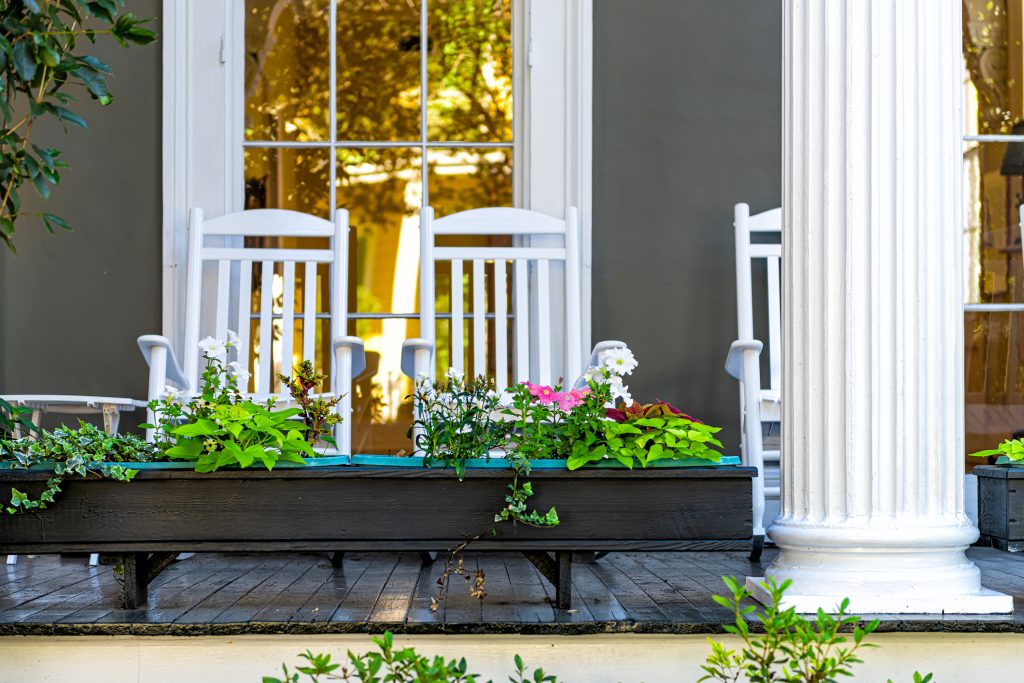 patio garden green plants flowers, white antebellum column and rocking chairs by mansion house